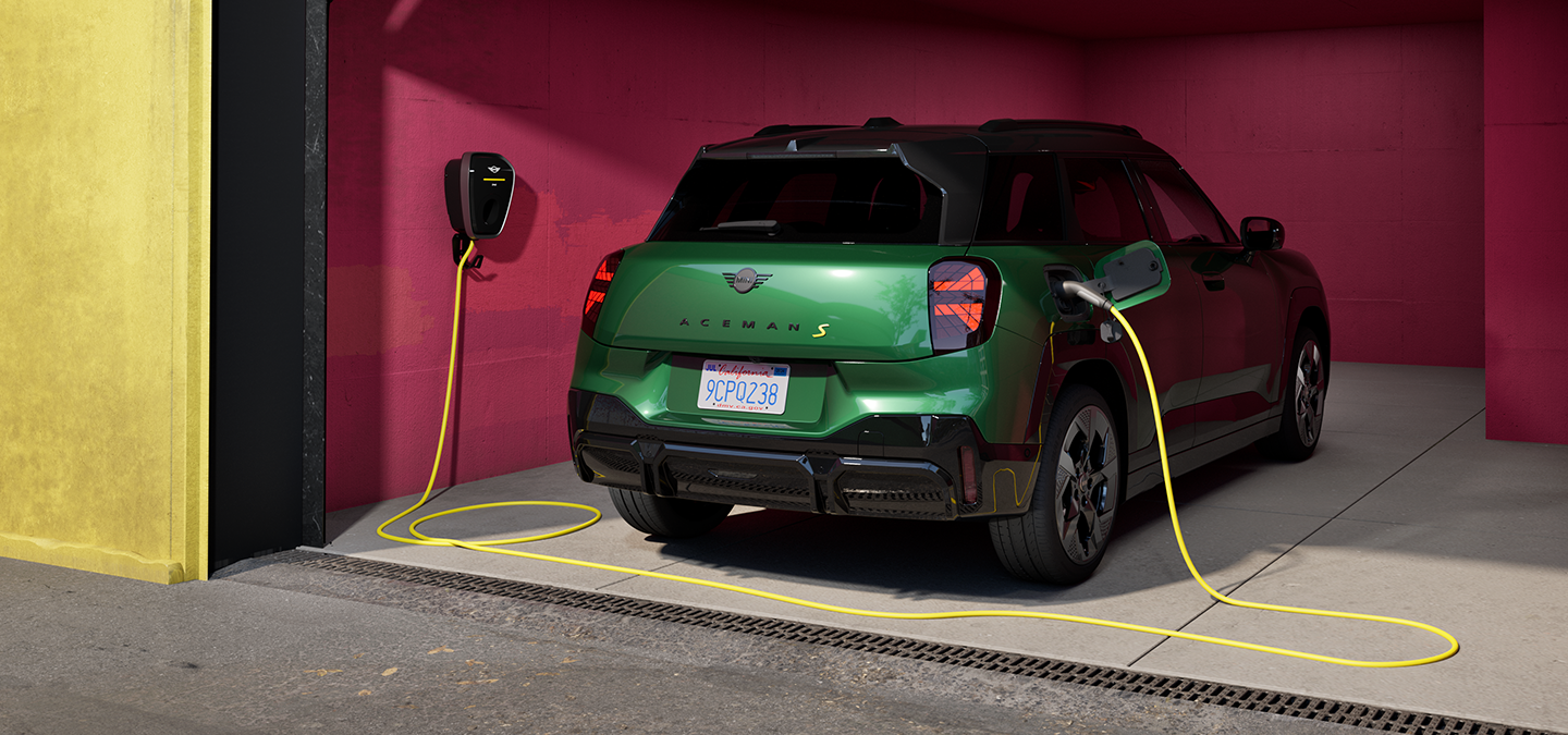 Den helelektriske MINI Aceman i British Racing Green som lader i en garasje, sett bakfra. 