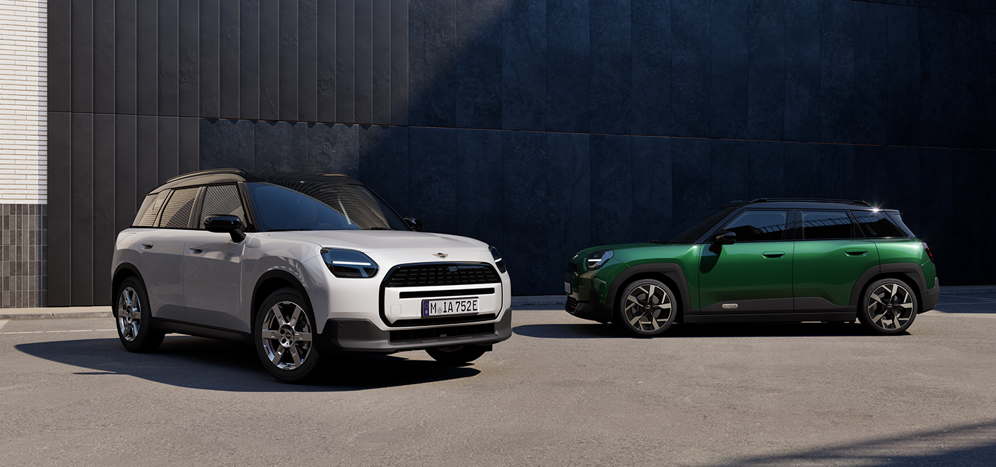 Den helelektriske MINI Aceman i Nanuq White og British Racing Green med svart tak i en gate sett forfra og fra siden.