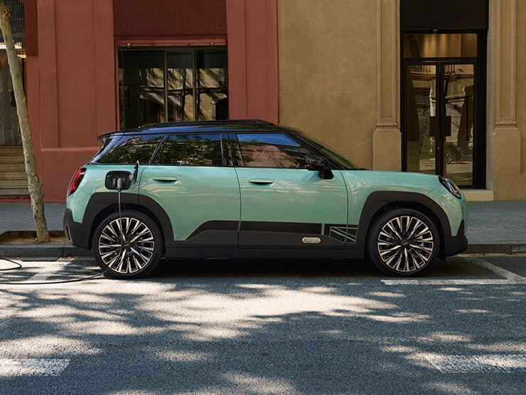 Den helelektriske MINI Aceman i Ocean Wave Green med svart tak, som lader på gaten, sett fra siden.