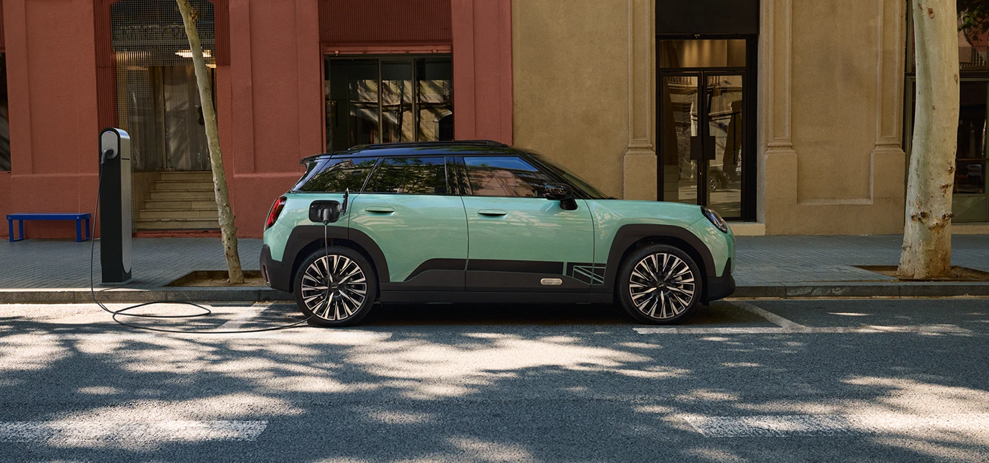 Den helelektriske MINI Aceman i Ocean Wave Green med svart tak, som lader på gaten, sett fra siden.