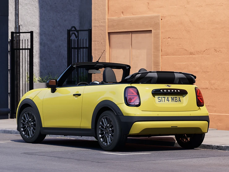 En MINI Cooper Cabrio i Sunnyside Yellow som parkerer, sett bakfra fra venstre side.