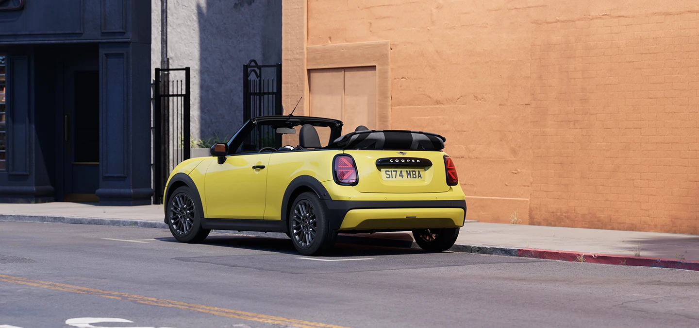 En MINI Cooper Cabrio i Sunnyside Yellow som parkerer, sett bakfra fra venstre side.