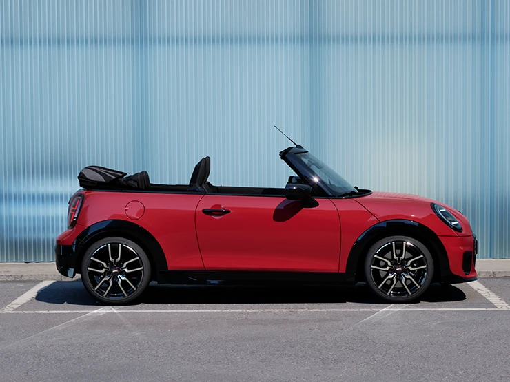 En MINI Cooper Cabrio i Chili Red på en vei, sett fra siden.