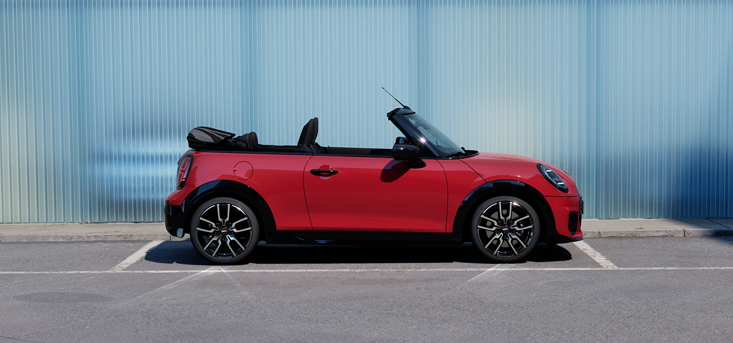 En MINI Cooper Cabrio i Chili Red på en vei, sett fra siden.