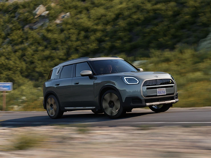 En terrengkjørende helelektrisk MINI Countryman i Smokey Green med tak i Vibrant Silver, sett fra siden.