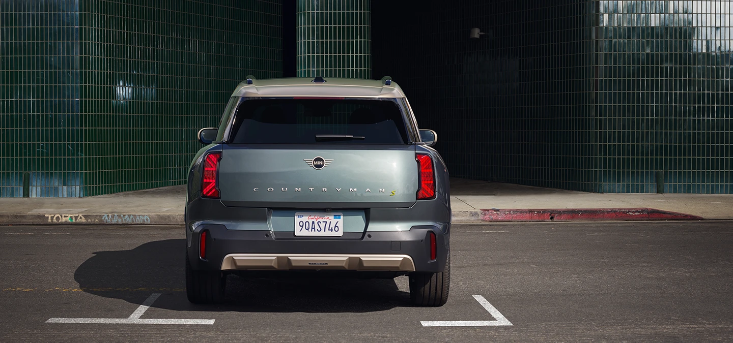 Helelektrisk MINI Countryman i Smokey Green med tak i Vibrant Silver som parkerer, sett bakfra. 