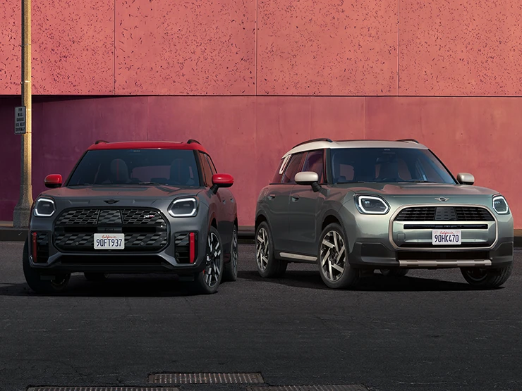 MINI Countryman JCW i Legend Grey med rødt tak og MINI Countryman i Smokey Green med tak i Vibrant Silver som står ved siden av hverandre, sett forfra.