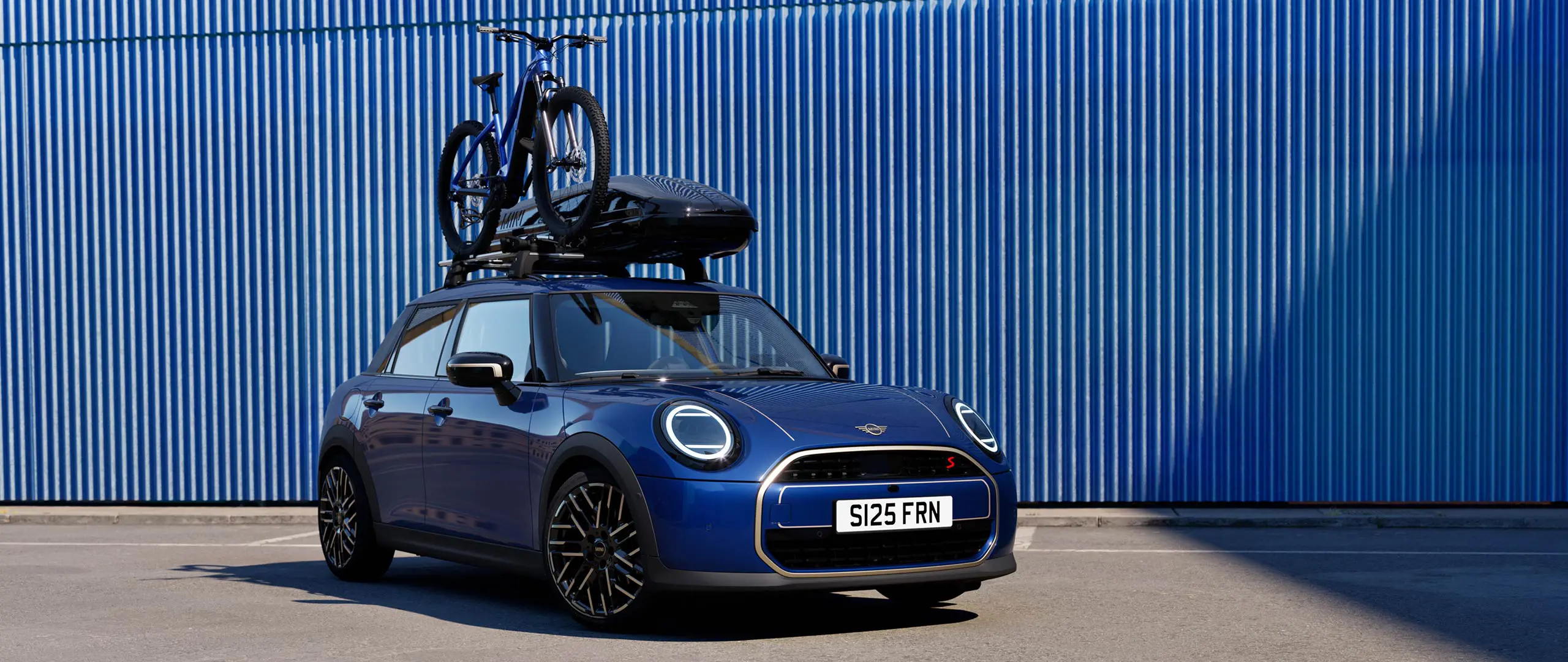 MINI Aceman i Indigo Sunset blå med MINI taksykkelstativ med terrengsykkel og MINI takboks 320 sett forfra.