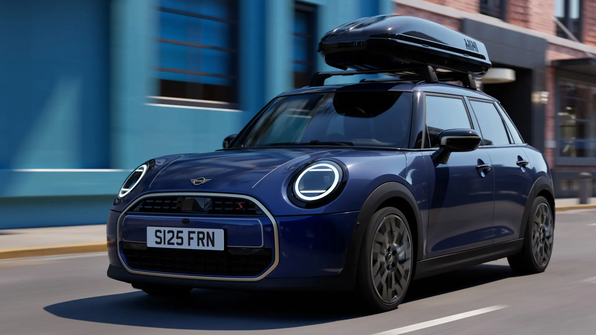 MINI Aceman i Indigo Sunset blå med MINI takstativ og MINI takboks 320 sett tre kvart forfra. 