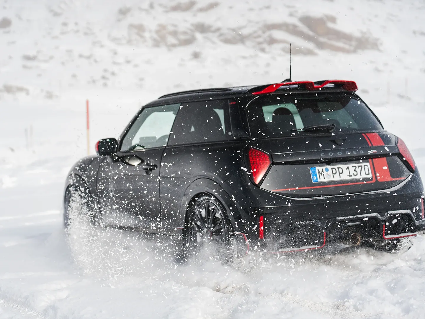 MINI Cooper JCW kjører gjennom snøen, sett bakfra.